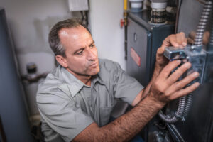 A middle aged man wearing a gray uniform focuses on installing a propane furnace.